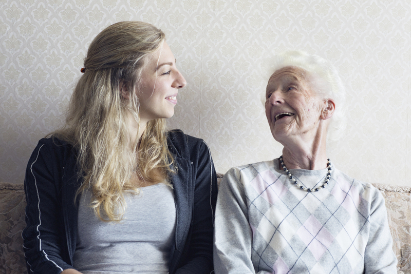 Enkelin und Oma sitzen auf Bank und lachen sich gegenseitig an