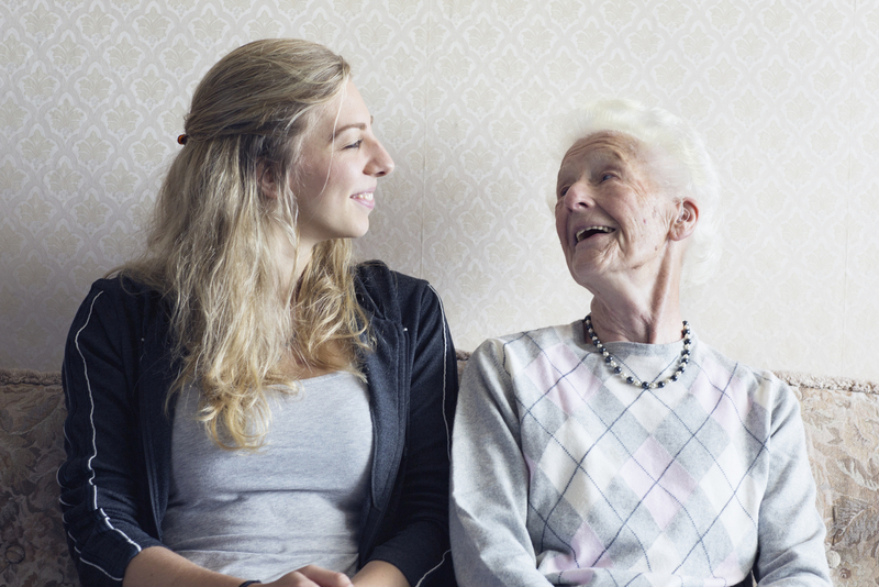 Enkelin und Oma sitzen auf Bank und lachen sich gegenseitig an