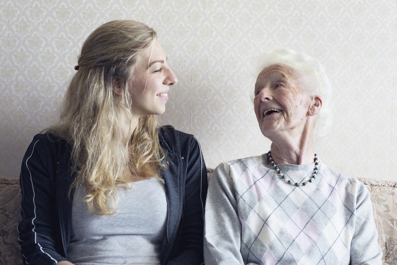 Enkelin und Oma sitzen auf Bank und lachen sich gegenseitig an