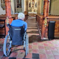 Eine Person im Rollstuhl blickt auf den Altar einer Kirche.