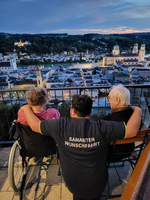 Drei Personen genießen die Aussicht auf eine Stadt bei Sonnenuntergang.