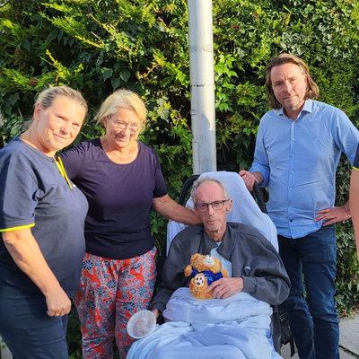 Vier Personen stehen um einen Mann im Rollstuhl, der ein Plüschtier hält.