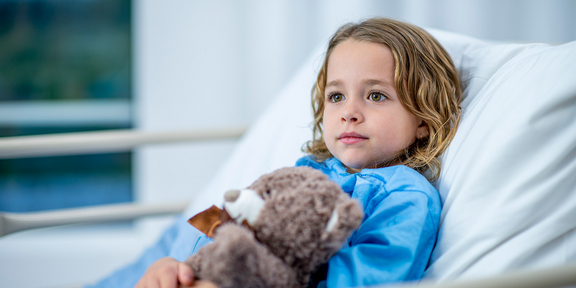 Kind im Krankenhausbett mit Teddybär