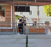 Eine Person macht ein Herzzeichen mit den Händen auf einer Terrasse.