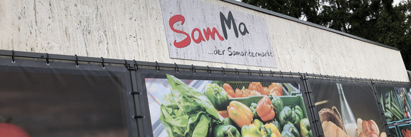 Marktgebäude mit dem Schriftzug „SamMa – der Samartmarkt“ und frischem Gemüse.