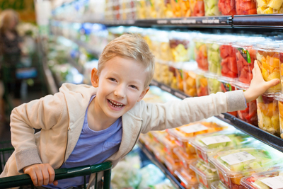 Kleiner Junge greift zu frischem Obst in Supermarkt-Regal