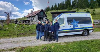Gruppe von fünf Personen steht neben einem Van in einer Landschaft.