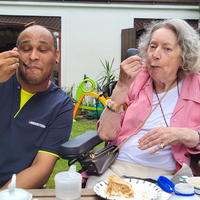 Zwei Personen genießen Kuchen und Kaffee in einem Garten.
