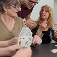Drei Personen spielen Karten und lachen zusammen an einem Tisch.
