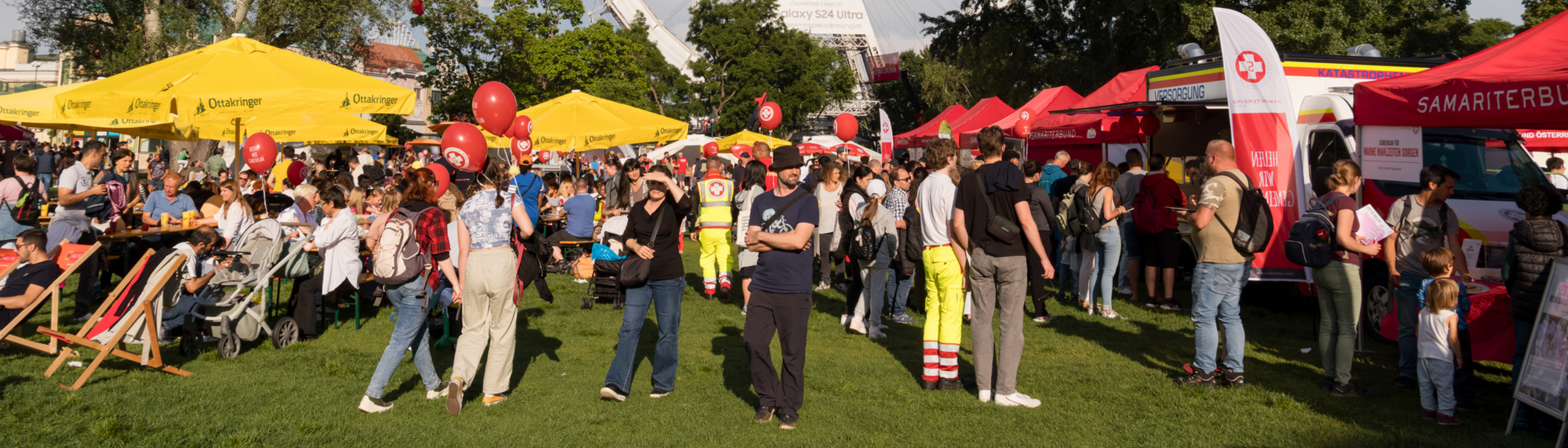Menschen genießen ein Fest mit einem Riesenrad im Hintergrund und bunten Ständen.