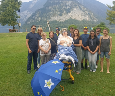 Gruppenfoto von Menschen, die eine Person im Rollstuhl am See besuchen.