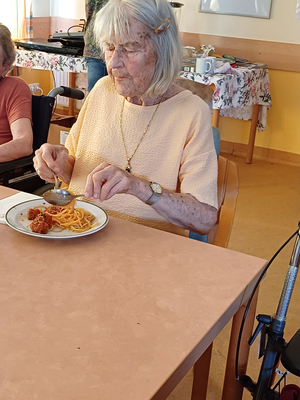 Eine ältere Frau isst Spaghetti und Fleischbällchen am Tisch.