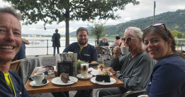 Vier Personen genießen Kaffee und Kuchen in einem Café am Wasser.