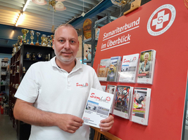 Mann hält Informationsmaterial des Samariterbunds vor einem Plakat.